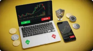 パソコンにチャートが表示され、スマホとコインが横に置かれている